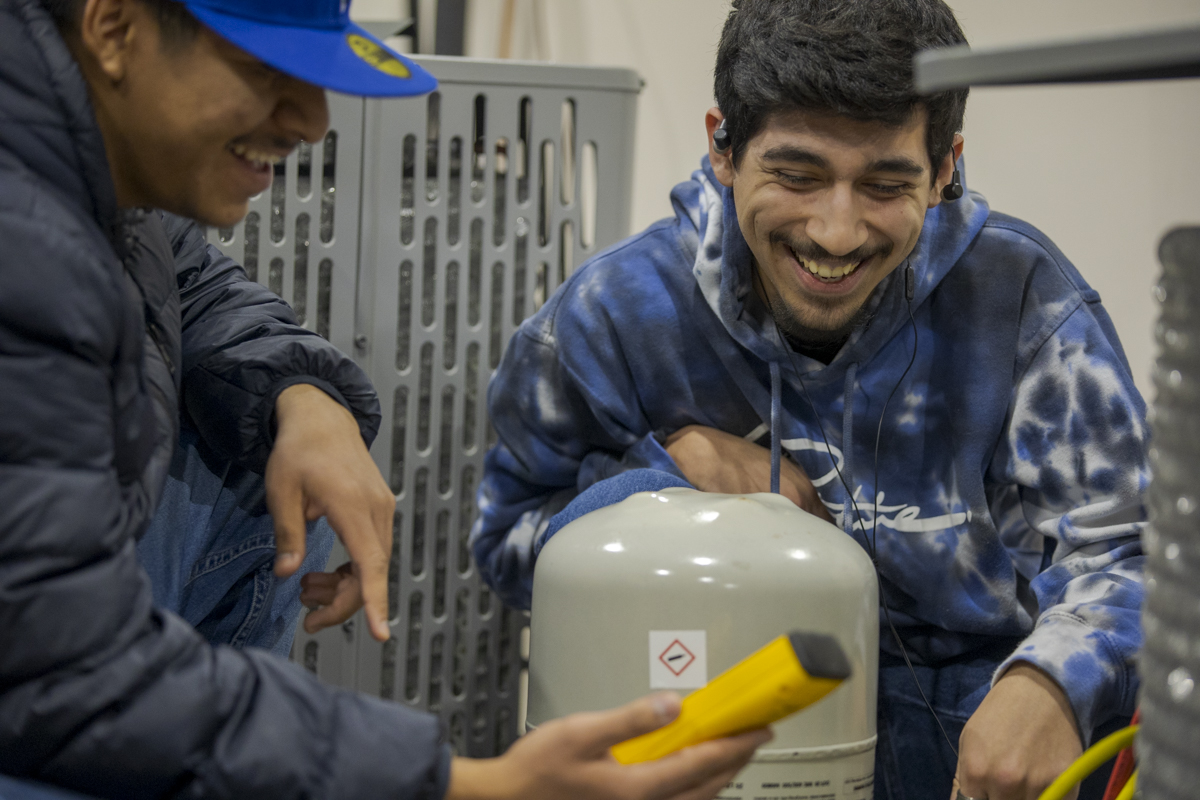 Two Male HVAC Students Smile as They Look at Equipment in HVAC Lab in Denver, CO