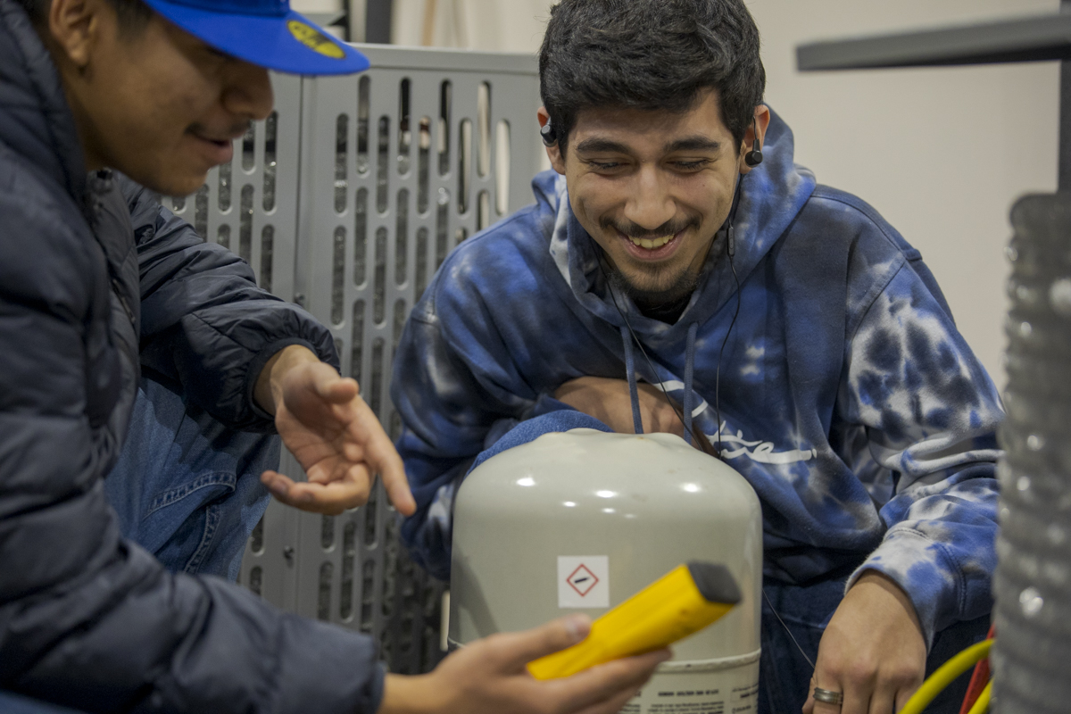 Two Male HVAC Students Smile as They Look at Equipment in HVAC Lab in Denver, CO