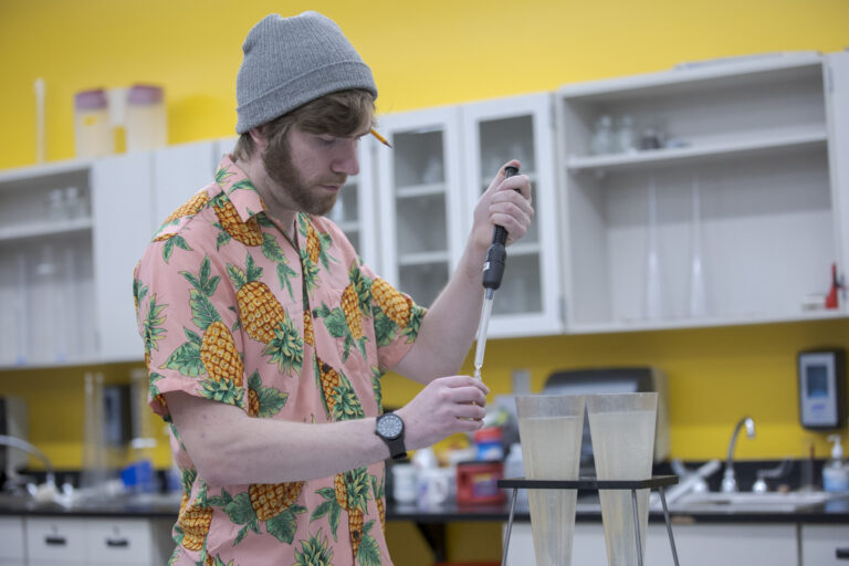 Male Water Quality Management Student in Pineapple Shirt Tests Water with Dropper and Beaker in Denver, CO