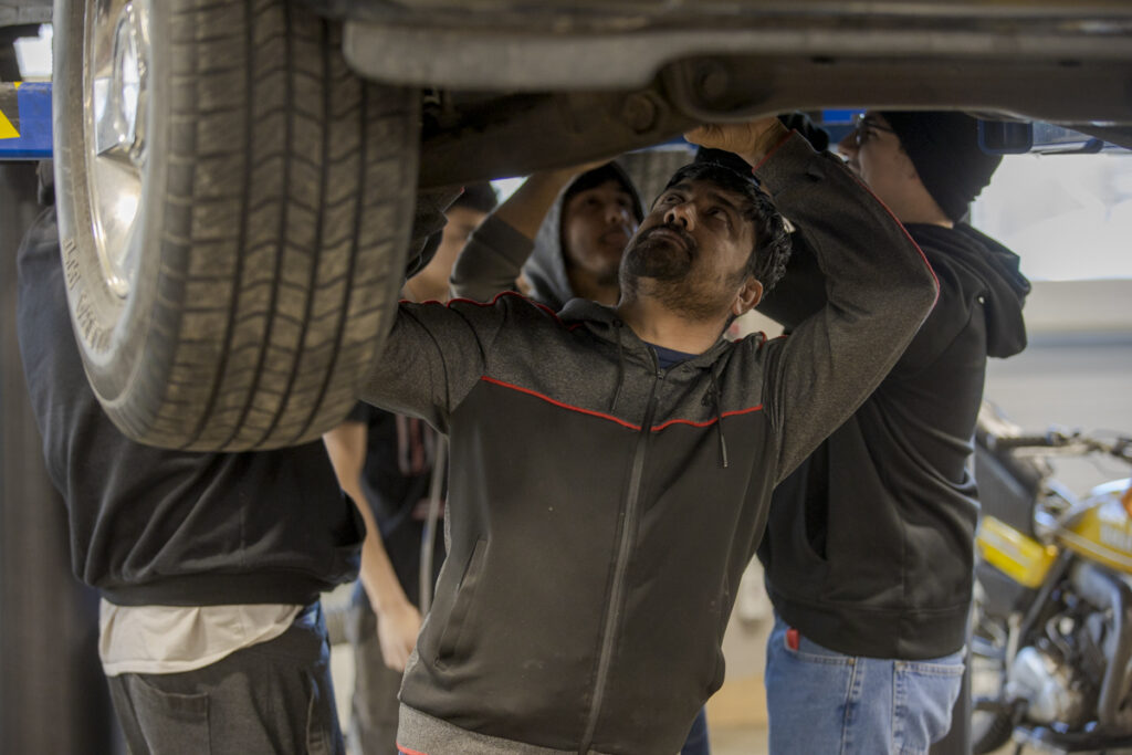 Male Automotive Service Student Working Underneath Vehicle in Denver, CO