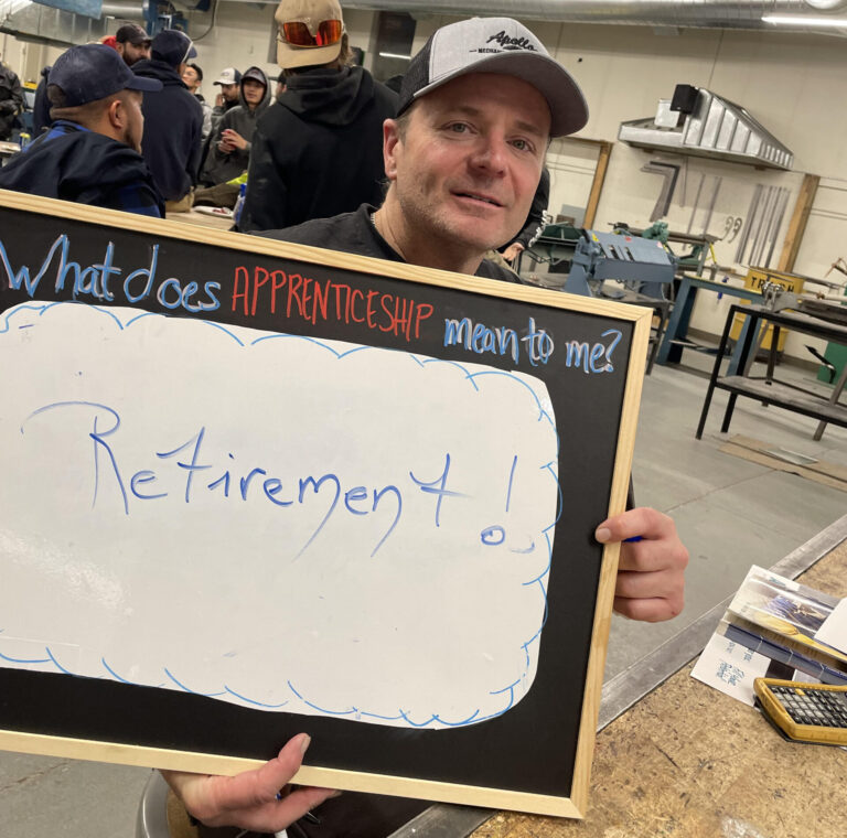 Apprenticeship student smiling while holding a board asking "what does apprenticeship mean to me?" Student's answer is "retirement"