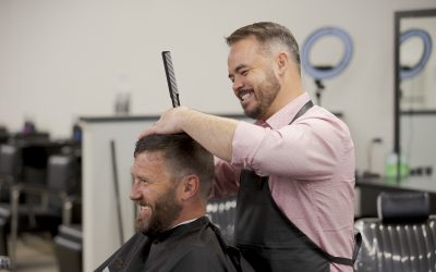 Barbering student smiling as they style a smiling client's hair